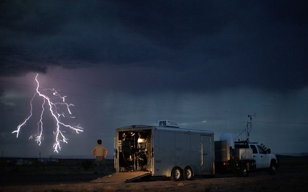 A weather researcher looks on as the sky lights up with a cloud-to-ground lightn