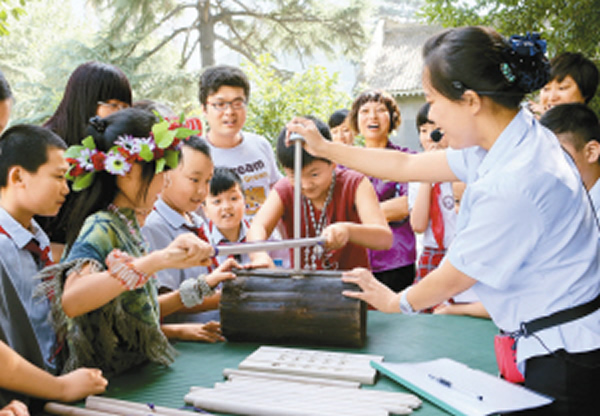小学生们在“周口店遗址巡展——走进半坡”展厅外体验“北京人”如何钻木取火