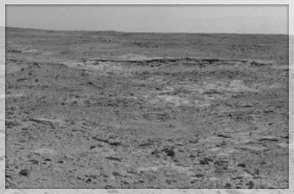 在这个场景的中间位置,位于地平线前方的一道低矮的隆起看起来像是一条黑带子,这道隆起就是火星上的露出岩“库珀斯敦”,这里可能是美国宇航局的“好奇”号利用机械臂上的