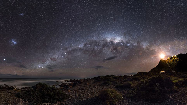 银河系的中心地带,距离地球约2.6万光年,充满了尘埃和无数的小恒星。新西兰帕利斯尔角的一座灯塔照亮了昏暗的银河系,点点星光闪耀在海面上,浪漫异常。