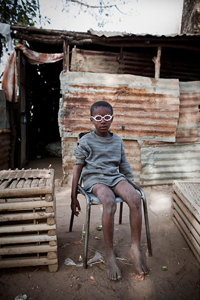 冈比亚河沿岸乔治小镇里的一个男孩,坐在母亲的咖啡店外,带着塑料眼镜玩耍。