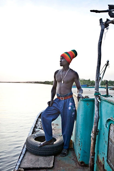 一位年轻的水手站在自己的拖船上,准备把内地农场的花生运到冈比亚首都班珠尔去。