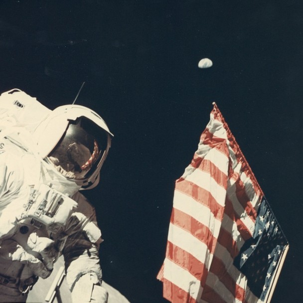 美国太空人将国旗置于地上,地球在天空高挂。