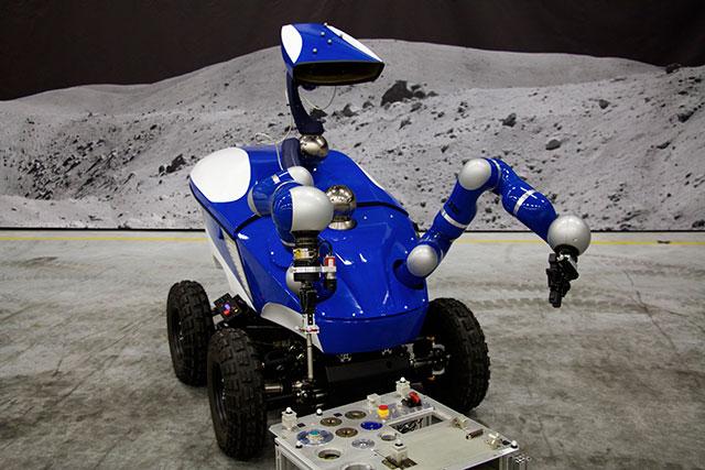 欧空局空间研究与技术中心(ESTEC)内的机器人漫游车“蓝虫”，背景图是灰色的月球山丘，它在国际空间站宇航员的操作下完成了此次试验。
