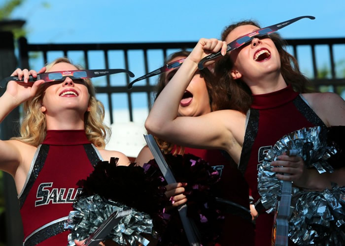 大学啦啦队少女暂停排练,在运动场上观看日食。